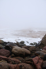 foggy beach with rocks in snow and ice at winter