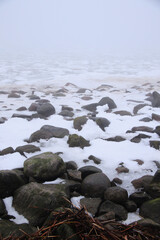 foggy beach with rocks in snow and ice at winter