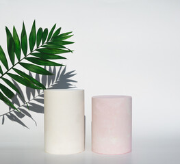 Empty podiums of cylinder shape on white background with shadow and  tropical green leaf for product.  