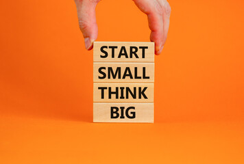 Start small think big symbol. Concept words 'Start small think big' on wooden blocks on a beautiful orange background. Businessman hand. Business, motivational and start small think big concept.