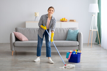 Pretty young lady wiping floor with mop, doing house cleanup, free space. Professional sanitary service concept