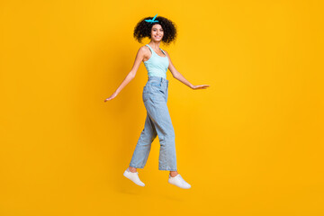 Photo of funny adorable curly woman wear teal singlet jumping high arms sides isolated yellow color background