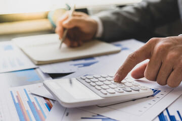 Fototapeta premium Asian male finance staff is calculating the investment results to deliver a report to his supervisor at the meeting. On the table in the office, the concept of calculating investment results