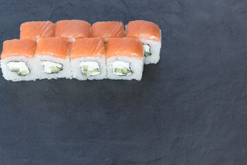 Rolls with salmon on a black stone board. Serve the dish. Rice, fish, avocado.