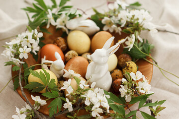 Modern easter eggs with spring flowers and bunny in wooden bowl on rustic linen. Happy Easter!