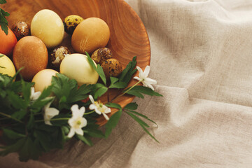 Modern easter eggs in wooden bowl with spring flowers on rustic linen cloth. Happy Easter! Aesthetic