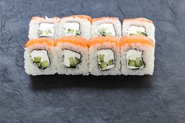 Rolls with salmon on a black stone board. Serve the dish. Rice, fish, avocado.