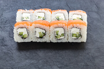 Rolls with salmon on a black stone board. Serve the dish. Rice, fish, avocado.