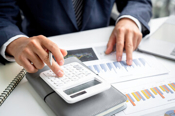 A close-up of an Asian male finance man's hand pressing a calculator on a desk in an office.