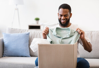 African Man Receiving Clothes Unpacking Box Holding T-Shirt At Home