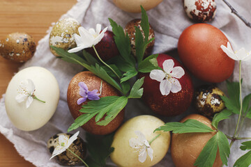 Modern pastel easter eggs with spring flowers on rustic linen cloth on wooden table. Happy Easter!