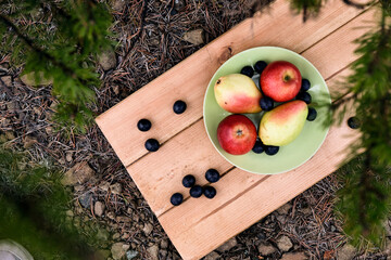 Apples, pears, grape lies on a green plate on a wooden stand. Cozy picnic on fresh air. Stone ground. Vegetarian healthy meal
