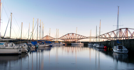 Fototapeta na wymiar The Red Forth Rail Bridge in the background and few boats from the boat club during sunrise.