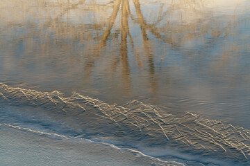 Foggy winter landscape at sunrise of the Kalamazoo River with ice formations and reflections in calm water, Michigan, USA