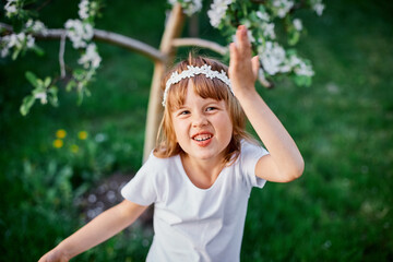 Portrait of funny kid girl 5-6 year old holding flower standing in blossom spring garden
