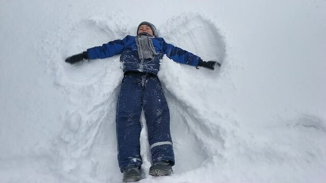 the boy is lying in a blue jacket in the snow. the image of an angel in the snow. winter entertainment.