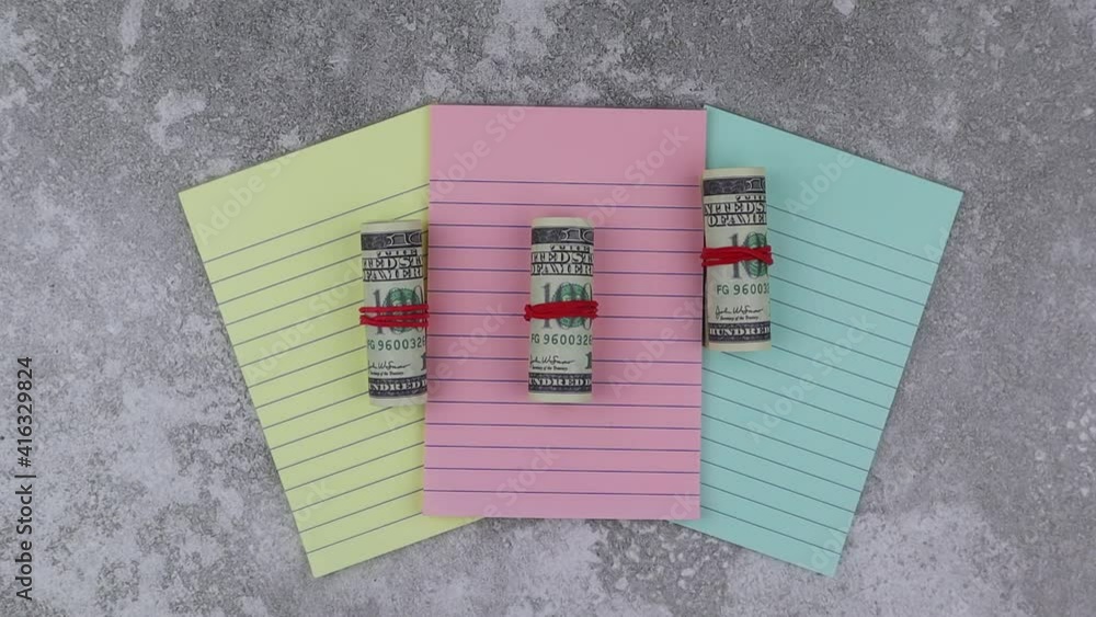 Poster rolls of 100 dollar banknotes on colored notepads arranged fanned to the centre of the screen on a w