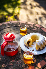 Picnic at springtime. Tea in cup and teapot with bundt cake on table outdoors. Serving dessert and hot drink in spring garden