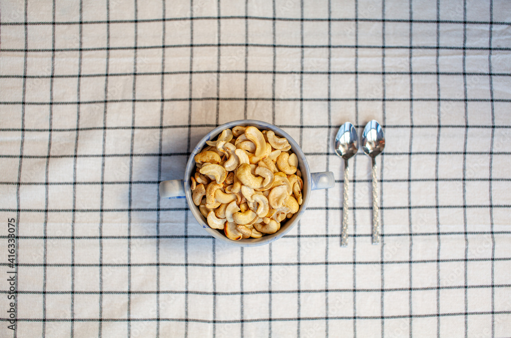 Poster a plate of cashew nuts on a nice napkin and two spoons next to it.