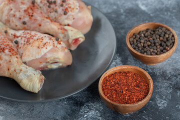 Close up photo of marinated raw chicken drumsticks with red and black pepper