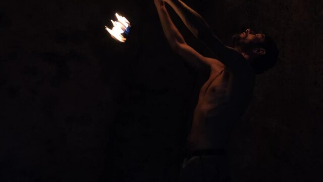 Medium shot of a man putting on a fire show, spinning fire balls in the darkness.