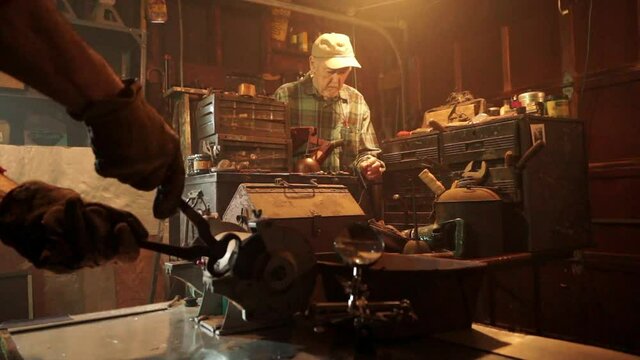 Elderly man works in workshop.  Tool is sharpened on bench grinder in foreground.
