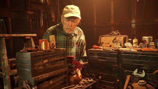 Camera jibs up on elderly man working at workbench.