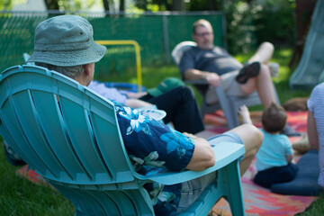 Two men sitting across from each other in Adirondack chairs in backyard; socially distant...