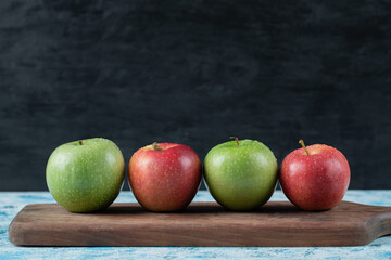 Red and green apples in a row on a wooden board