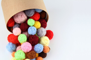Fototapeta na wymiar Lots of colorful, scattered wool balls of knitting yarn from a round cardboard gift box on a white background. The concept of handwork, needlework and needlework. Top view. Flatley. Copyspace.