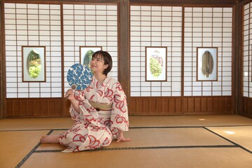 団扇を手に和室でくつろぐ若い笑顔の浴衣女性