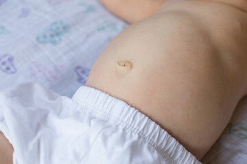 Young baby's stomach and belly button; child wearing diaper cover laying on muslin blanket