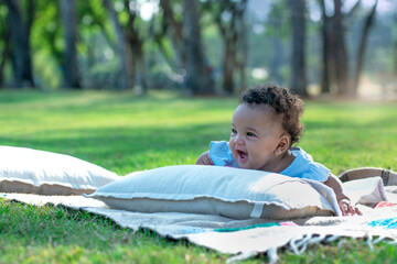 7 month old girl feels happy on the green grass outside in the summer garden, cosy picnic in public park