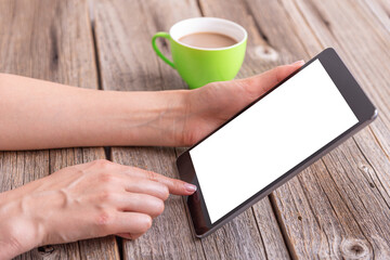 Tablet in hands on a wooden table with a cup of coffee.