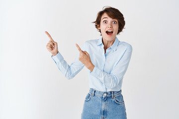 Impressed young caucasian woman open mouth fascinated, looking amazed and pointing at upper left corner logo, standing on white background