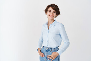Young working woman in office clothing, smiling and looking at camera, standing on white...
