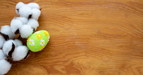 Dried white fluffy cotton flower and green egg on wooden background, close-up, copy space, top view. The concept of Easter. Space for your text