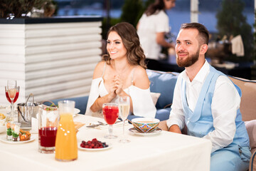 newlyweds sit at table in restaurant and listen to congratulations from guests.