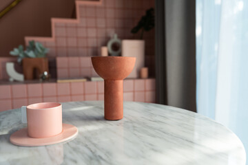Living room corner decorated with clay ceramic vase and baby pink cup on white marble  table with pink tile stair in the background. Copyspace
