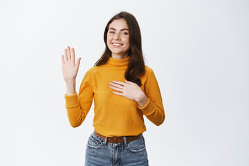 Smiling girl making promise, raising one hand and put another on heart, swear to be truth and be...
