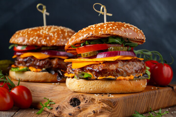 Two delicious homemade burgers of beef, cheese and vegetables on an old wooden table. Fat unhealthy...