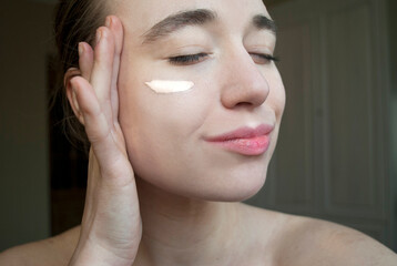 Young woman with bare shoulders and closed eyes applying foundation
