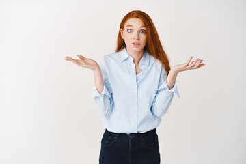 Confused redhead female hr manager shrugging, looking puzzled with hands spread sideways, standing against white background