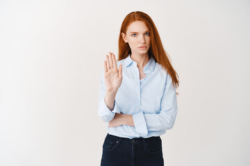 Serious business woman with red long hair telling to stop, showing rejection sign and frowning...