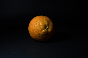 A ripe orange on a black background close-up.