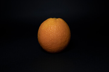 A ripe orange on a black background close-up.