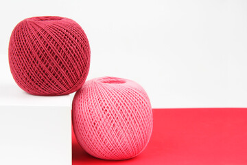 Crimson and pink tangles of cotton thread on a geometric red and white background. The concept of a favorite hobby of needlework, online knitting courses. Top view. Flatlay. Copyspace.