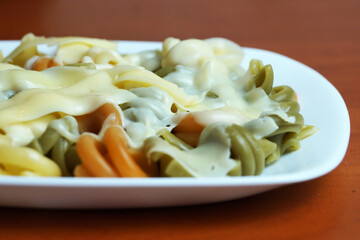 multicolored pasta with melted cheese on a white plate close-up