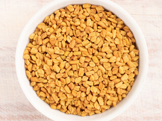 Spice fenugreek in a white bowl on a light wooden background