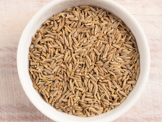 Spice cumin in a white bowl on a light wooden background
